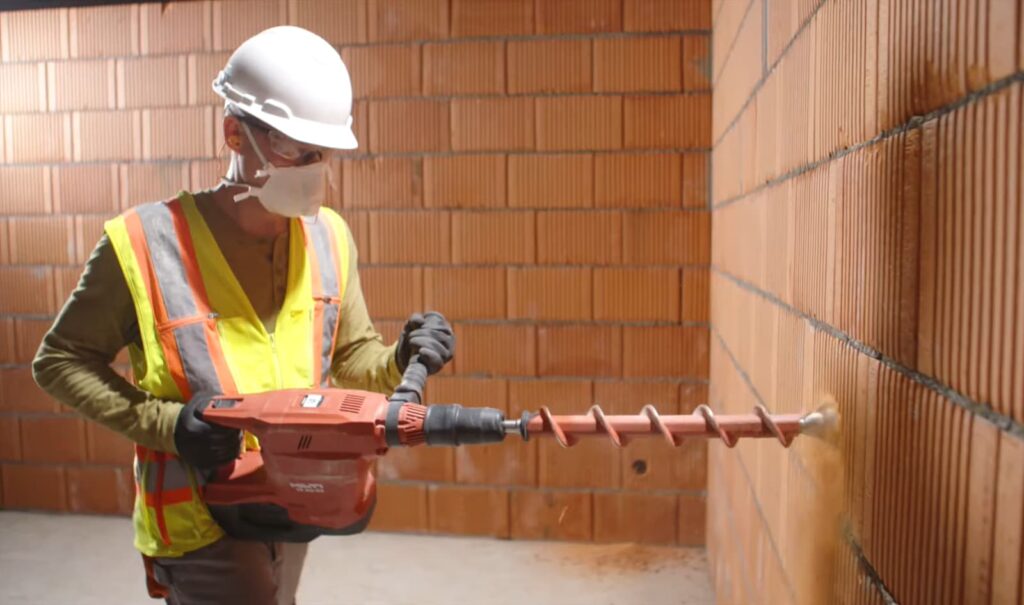 Ein Bauarbeiter bohrt mit einem Erdbohrer in eine Mauer