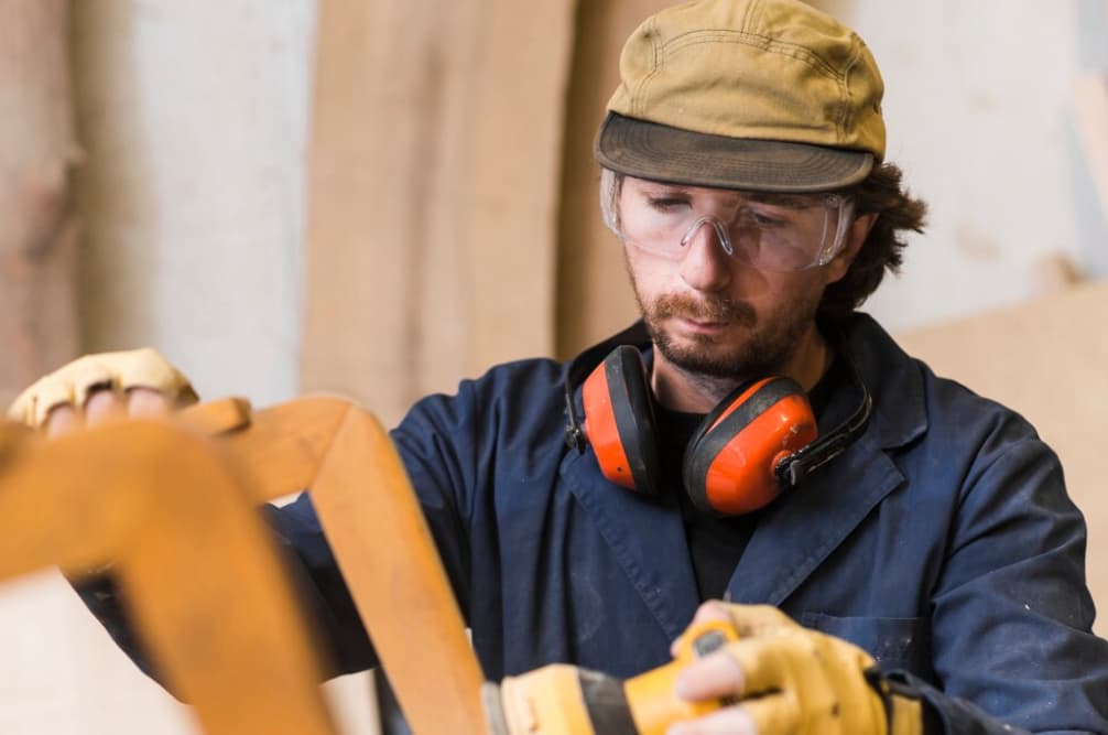 Mann mit Schutzbrille und Gehörschutz arbeitet mit Holz