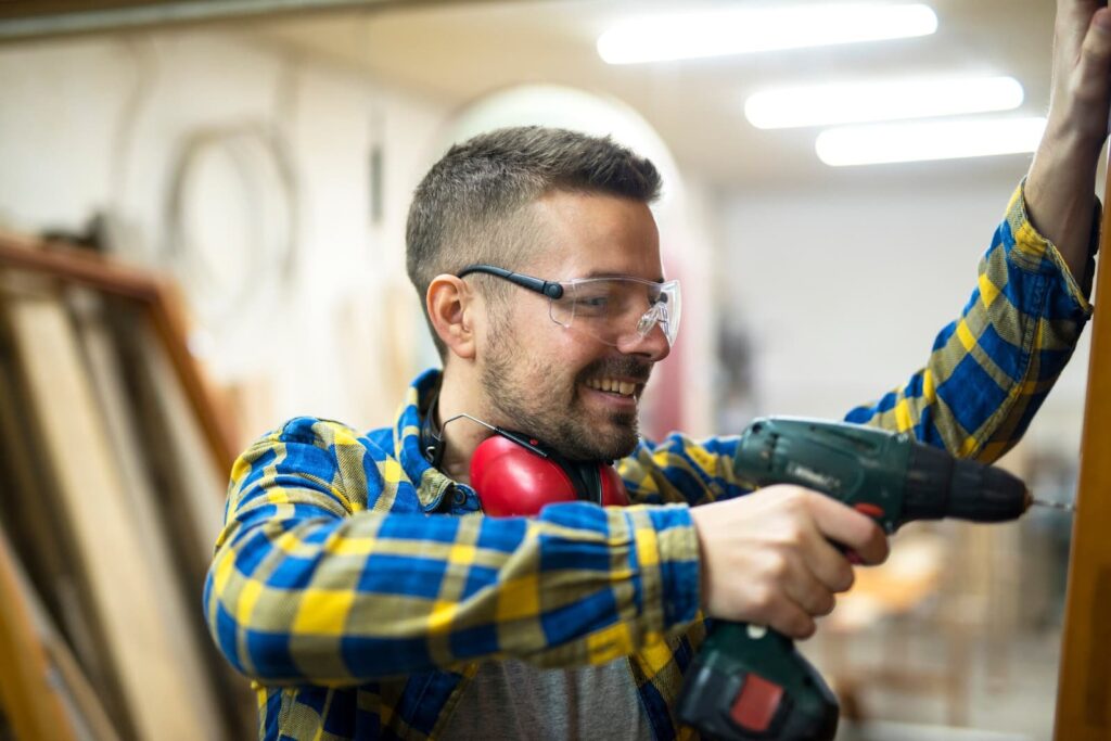 Ein Arbeiter mit Schutzbrille hält eine Bohrmaschine