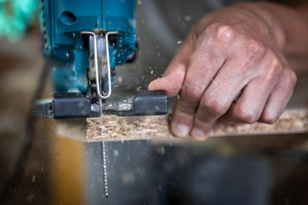 Hand bedient eine Elektrosäge, die Holz schneidet