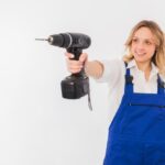 Eine Frau in Blaumann hält lächelnd einen Akkubohrer vor sich