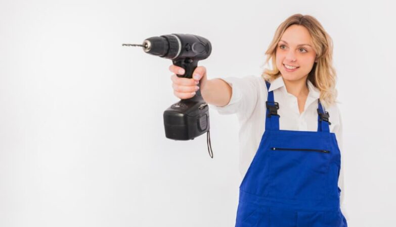 Eine Frau in Blaumann hält lächelnd einen Akkubohrer vor sich