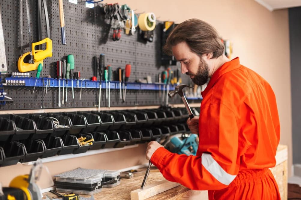 Ein Mann in orangefarbener Arbeitskleidung arbeitet konzentriert an einer Werkbank