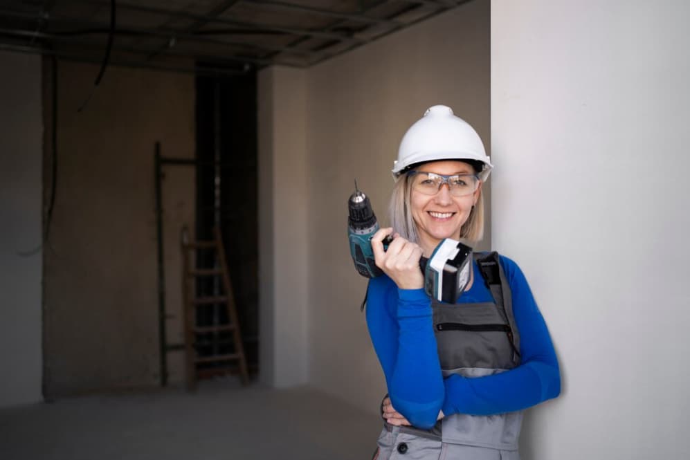 Lächelnde Frau mit einer Bohrmaschine auf einer Baustelle
