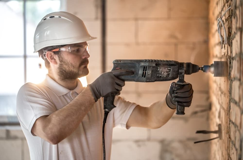 Mann mit Helm benutzt einen Bohrhammer an einer Wand