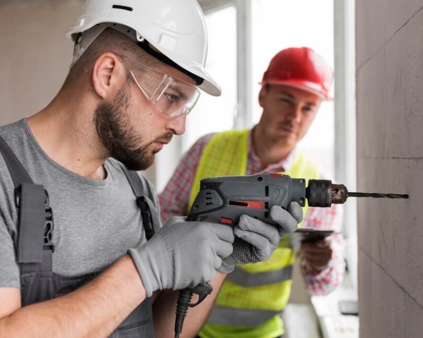 Ein Techniker benutzt einen Bohrer, ein Kollege notiert etwas