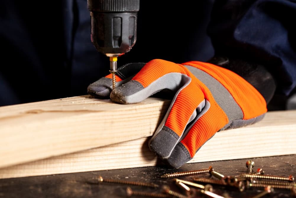 Eine Hand in einem orangefarbenen Handschuh benutzt einen Akkuschrauber